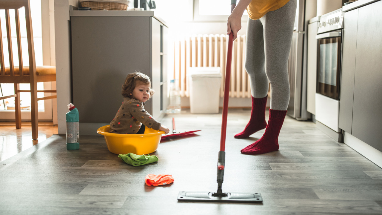 Ung mamma utför hushållsarbete medan ett litet barn tittar på.