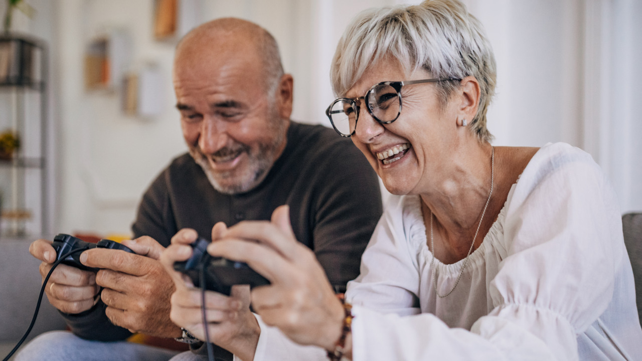 Medelålders par sitter i soffan och skrattar och spelar tv-spel